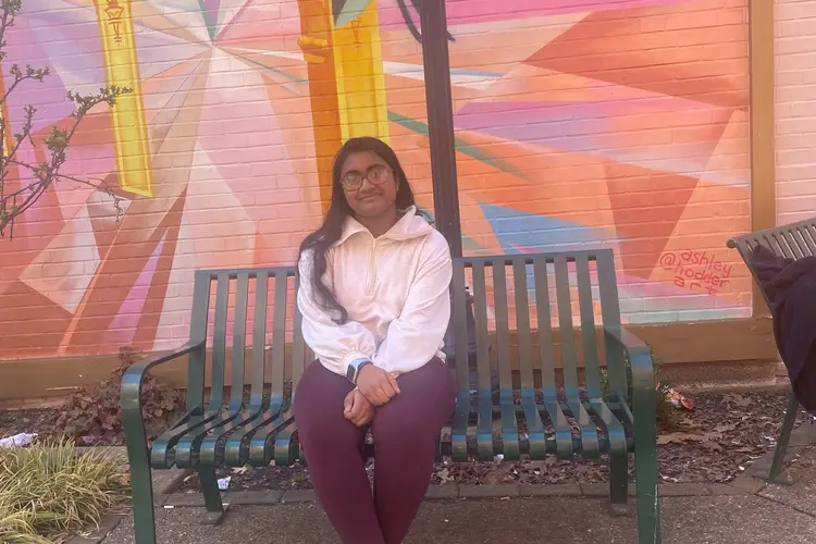 A photo of Samhita sitting on a bench in front of a mural in Shadyside.